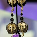 Trunked Majesty is a bold pair of clip-on earrings featuring detailed golden elephant heads with graceful trunks and decorative beads. Hexagonal black and gold patterns frame raised elephant motifs, blending luxury and strength in a regal, elegant design fit for a queen.